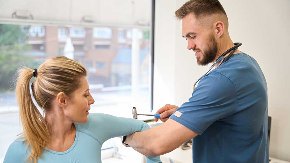 A fit blond woman has her reflexes tested by a doctor during a work physical