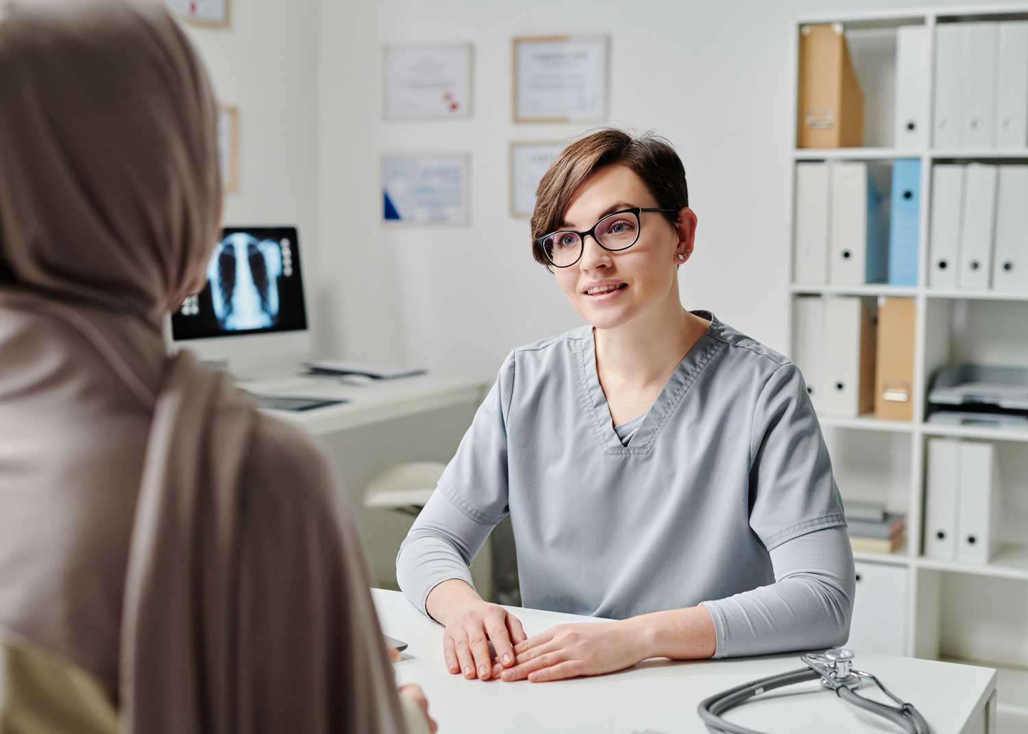 A woman sits on an exam table and talks to a nurse